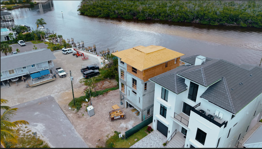 Aerial view of the four-story Bay Road residence shell on the water, roof sheathing complete